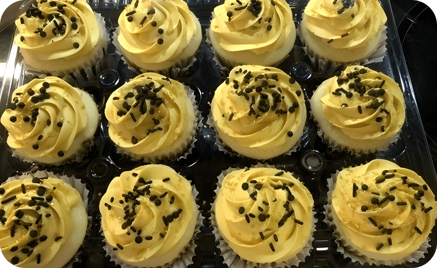 A tray of cupcakes with yellow frosting and chocolate sprinkles.