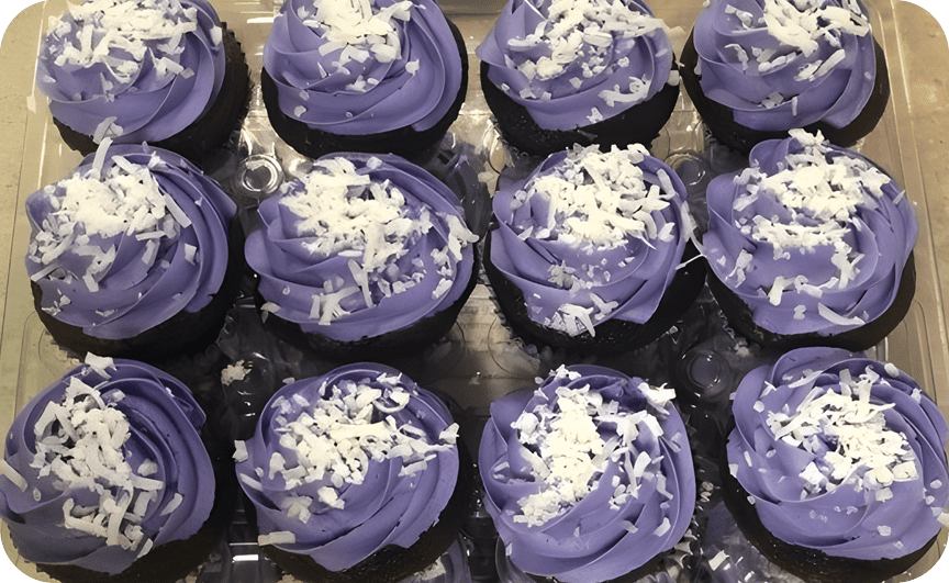 A tray of cupcakes with purple frosting and coconut shavings.