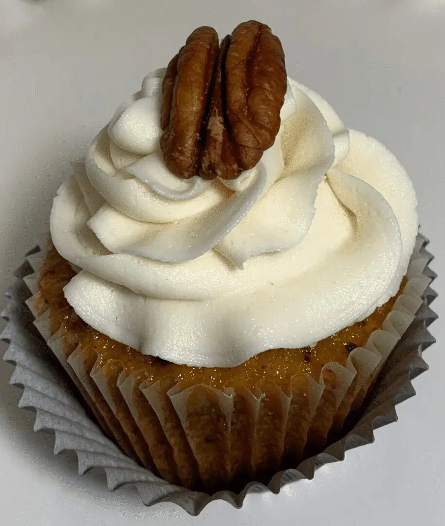 A cupcake with white frosting and nuts on top.