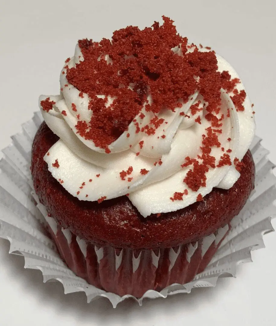 A red velvet cupcake with white frosting and sprinkles.